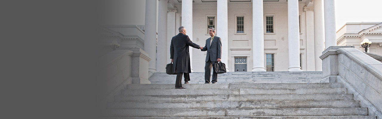 Image of two men shaking hands in front of a government building